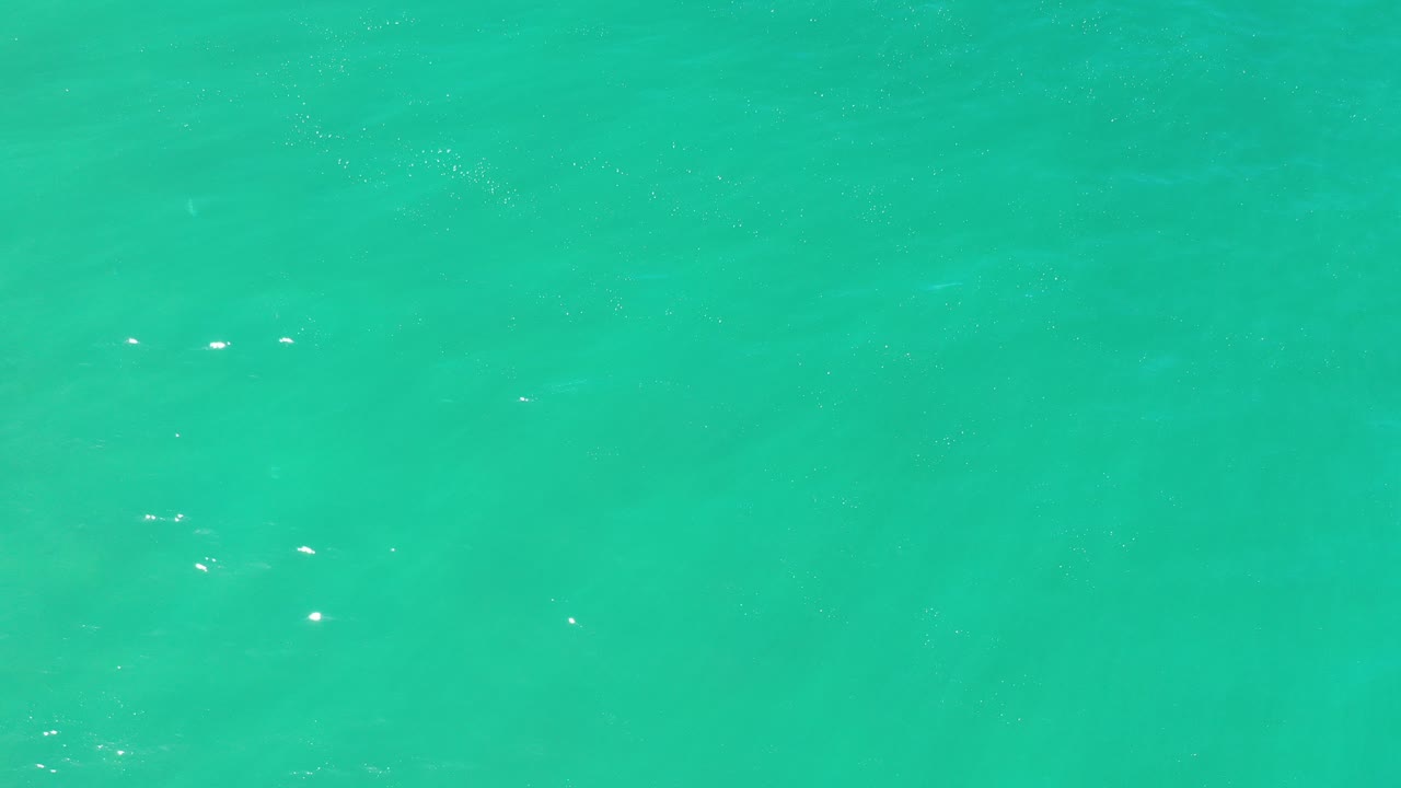 Turquoise green sea surface in Los Cabos, Mexico, with faint ripples, small white glints, and no visible people.