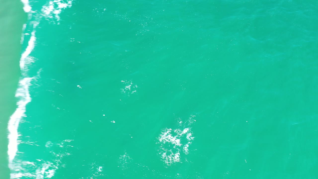 Bright teal ocean surface with a vertical white wave trail.