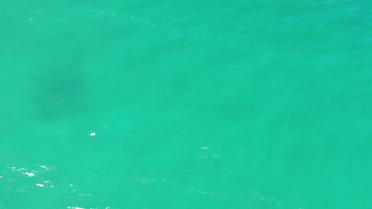 Turquoise-green shallow ocean water in Los Cabos fills the frame at the start of the clip, with faint bottom texture, small ripples, and no visible people.
