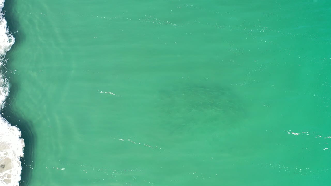Overhead green seawater with foam along a rocky left edge.