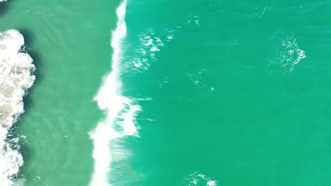Turquoise ocean with white surf breaking beside dark coastal rock.