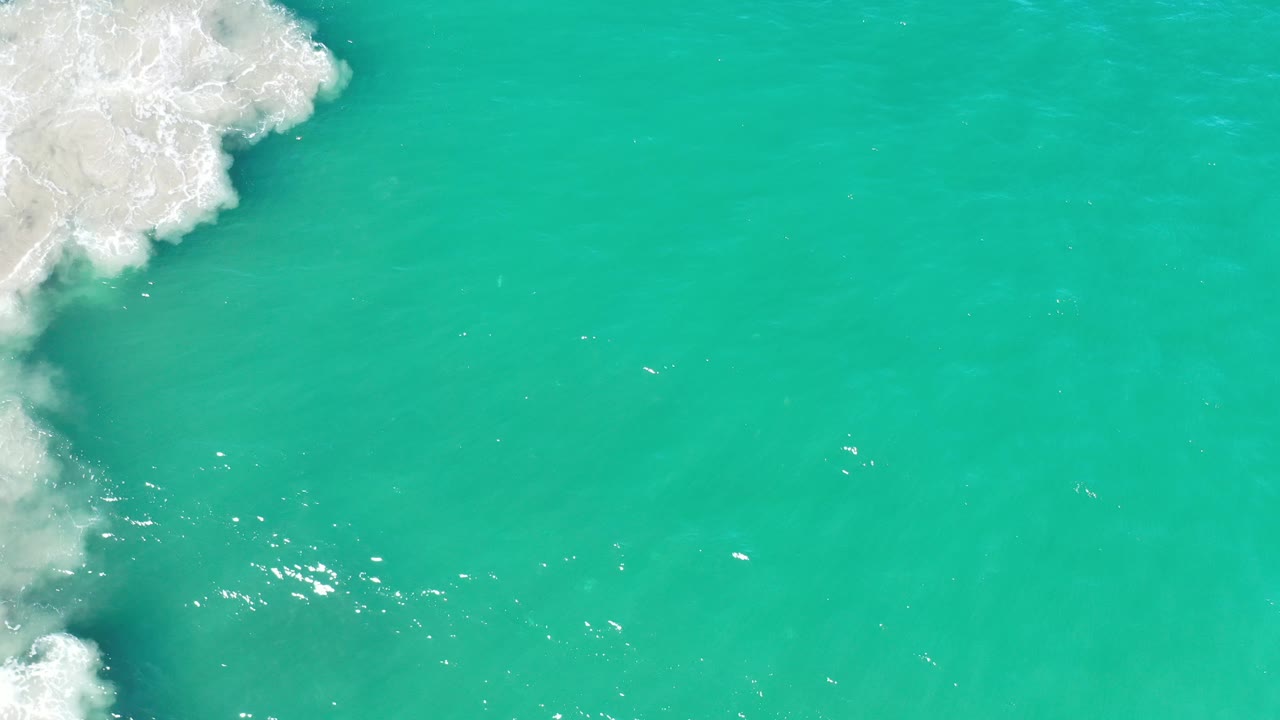 White foam at left beside smooth turquoise water.