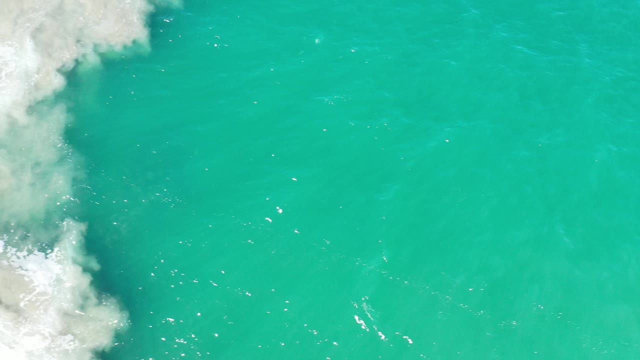 Turquoise ocean with a larger patch of white foam at left.