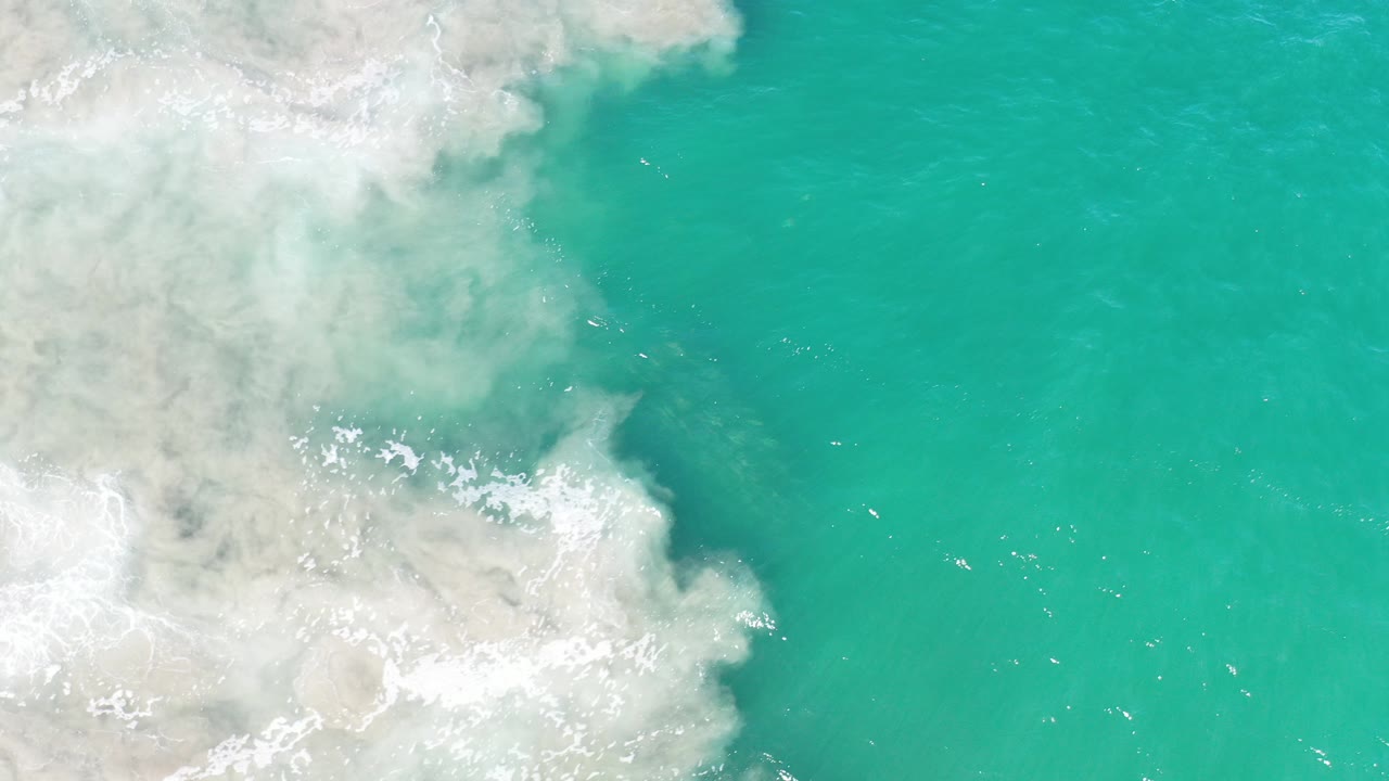 Overhead view of turquoise water and pale foamy surf along the Los Cabos shoreline, with no visible people.