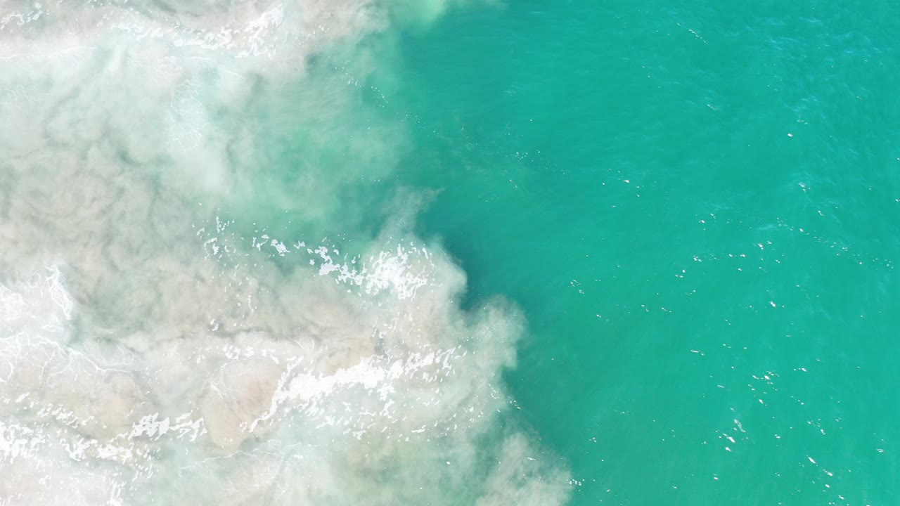 Overhead green ocean water mixing with pale sand and white foam.