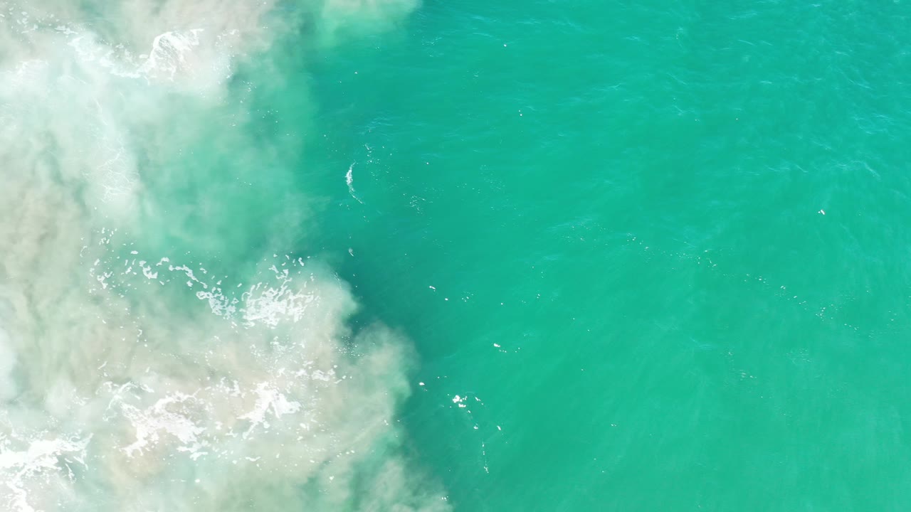 Aerial turquoise water with surf foam concentrated at upper left.