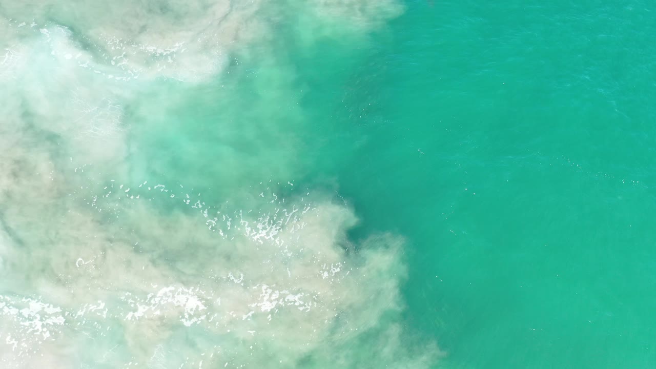 Foamy white water meets a broad area of clear green sea.
