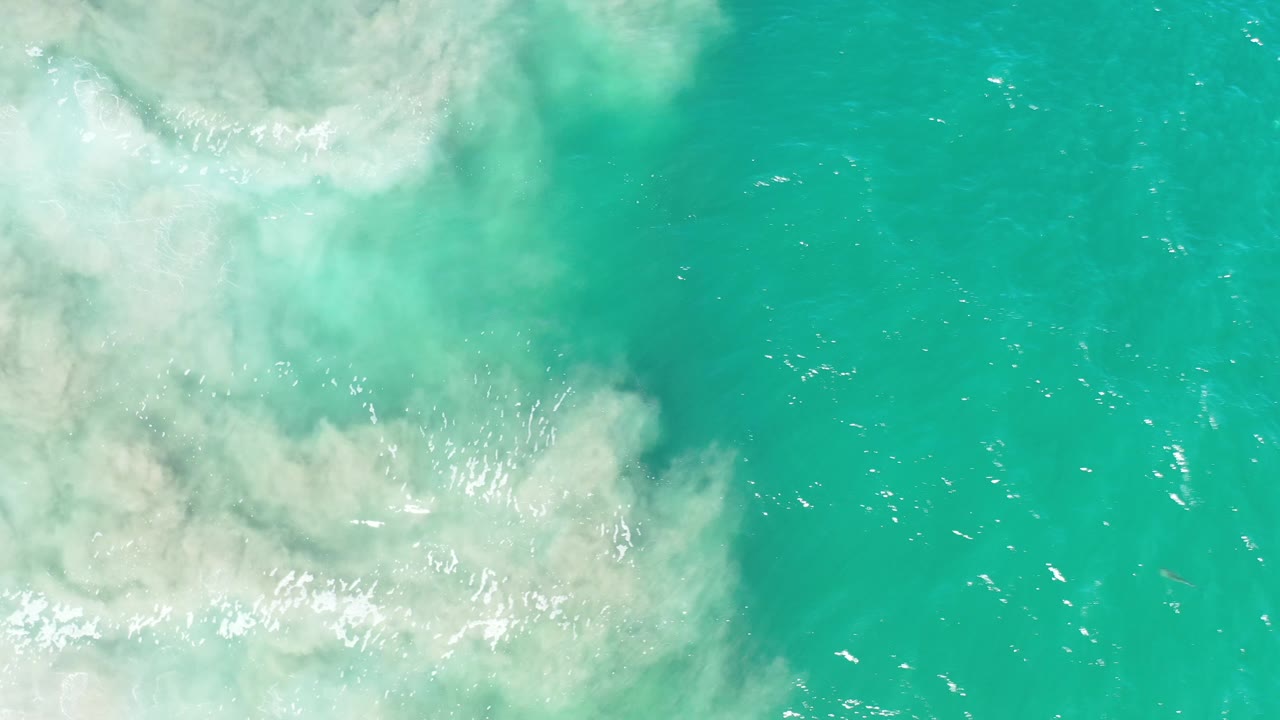 Foam and sandy clouding over bright green coastal water.