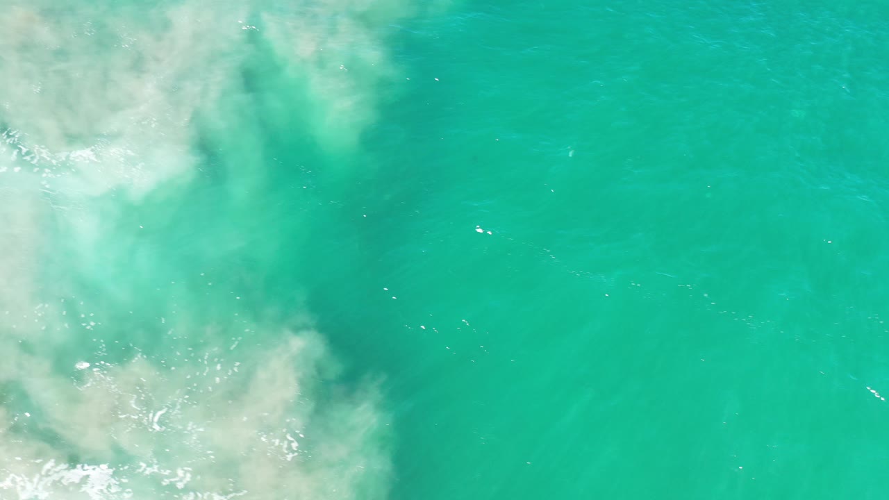 Overhead view of turquoise ocean water in Los Cabos, Mexico, with pale surf foam entering from the left side and no visible people.