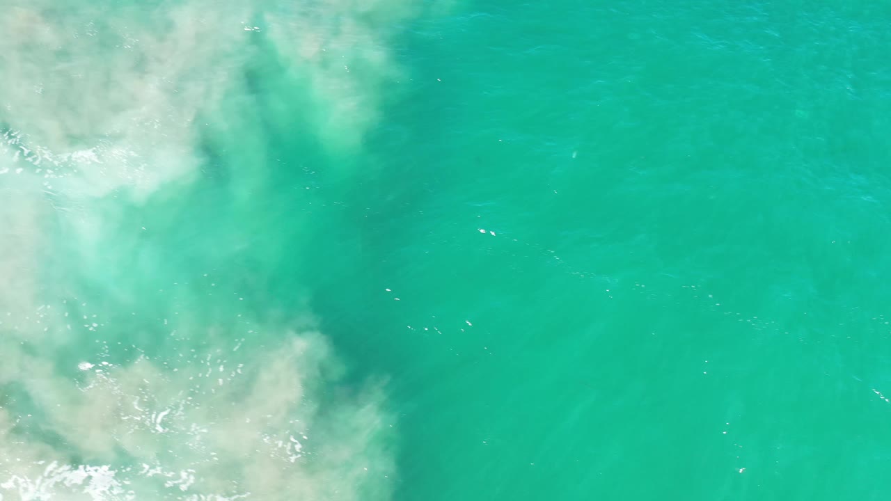 Clear blue-green water in Los Cabos, Mexico, fills the frame as diffuse white foam spreads along the left edge, with no visible people.