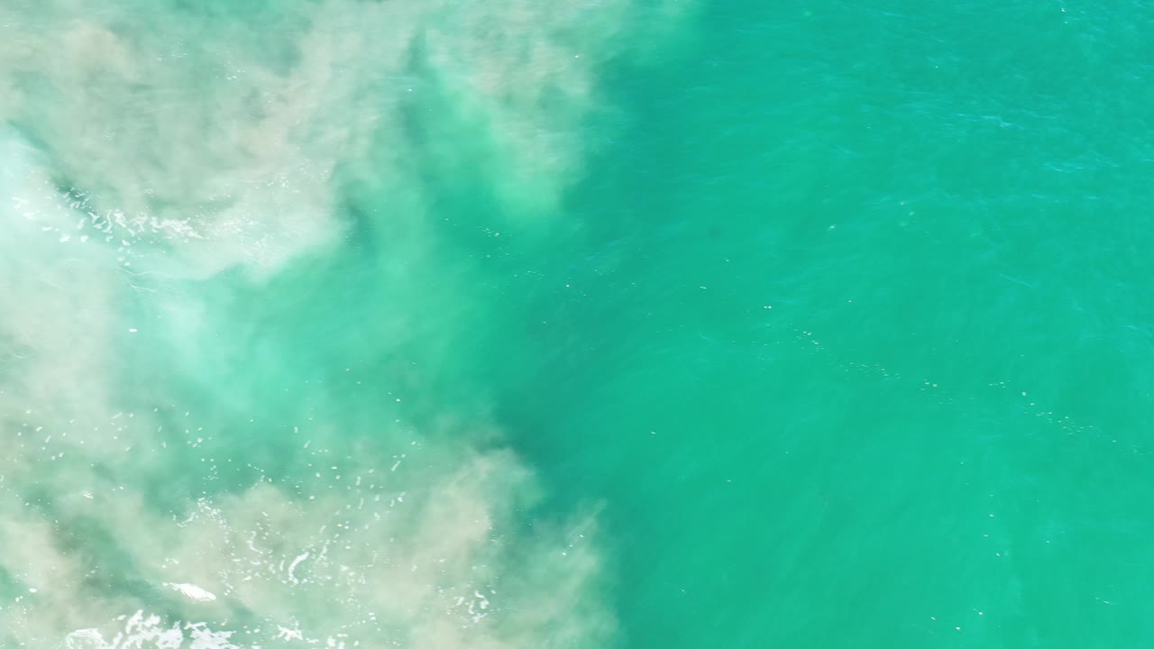 Turquoise sea surface with a broad pale foam cloud near the left side