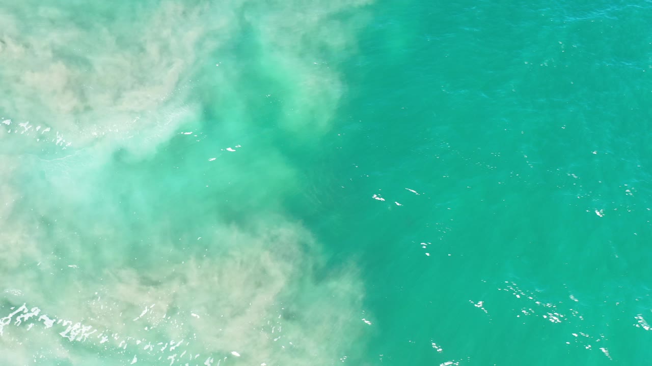 Overhead view in Los Cabos, Mexico, showing turquoise green water and pale sandy wash entering from the left, with no visible people.