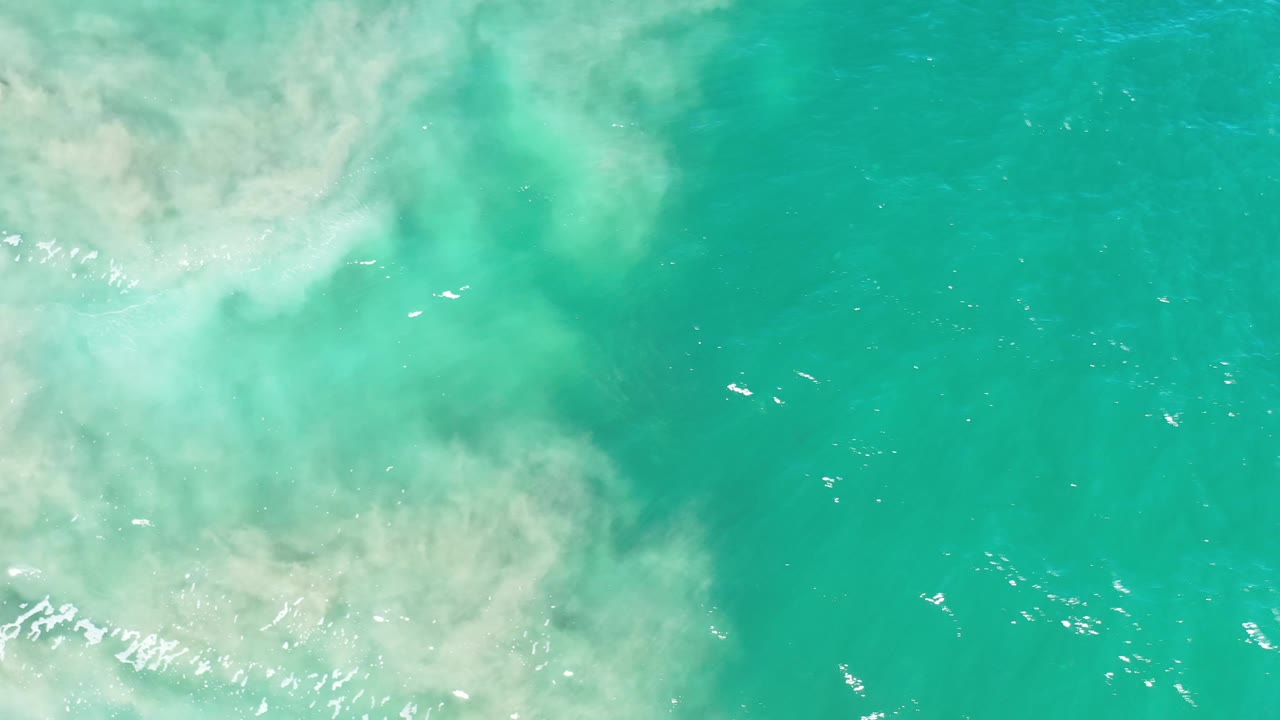 Aerial frame over Los Cabos water with a cloudy pale sediment plume across the left half and clearer green ocean on the right, with no visible people.