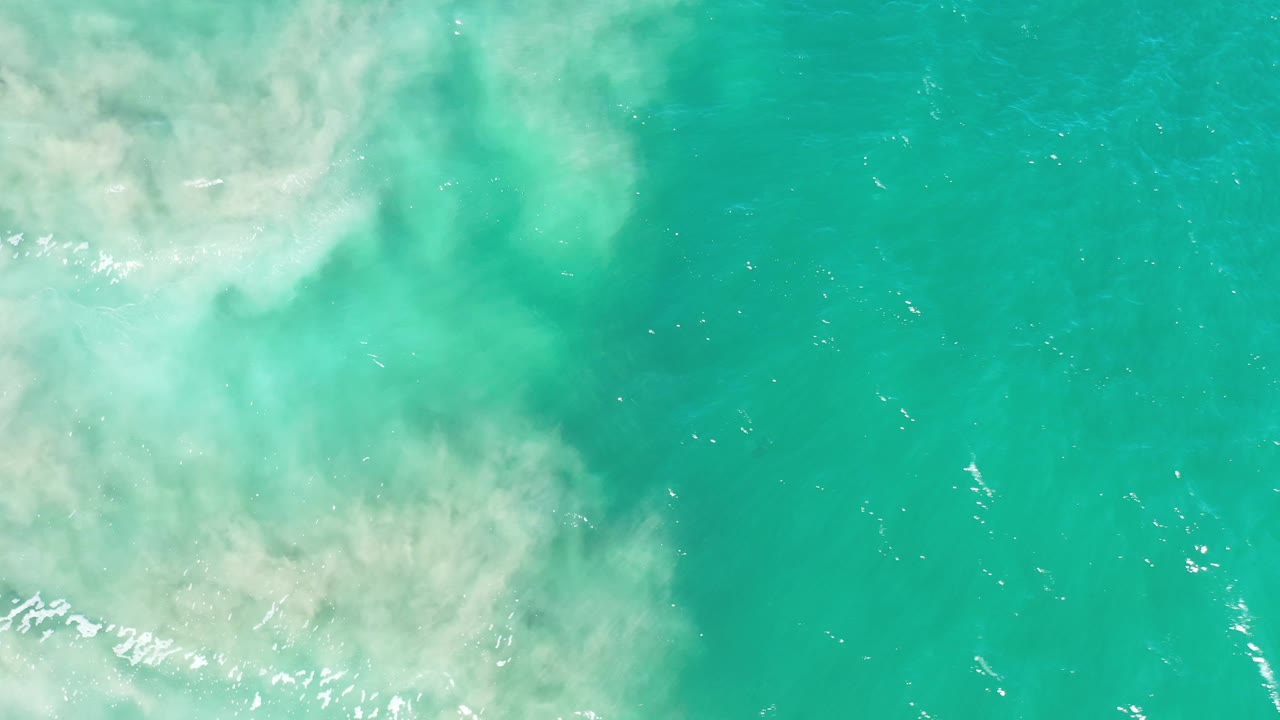 Green ocean surface with sandy wash at left