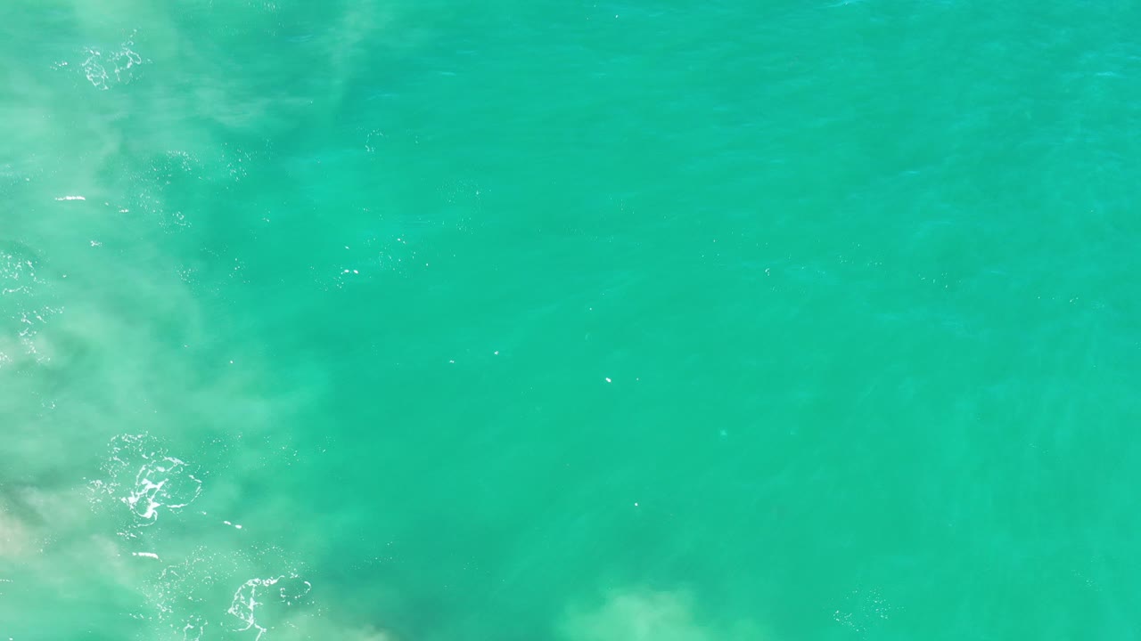 Overhead view of turquoise-green ocean water in Los Cabos, Mexico, with faint pale surf texture near the left edge and no visible people.
