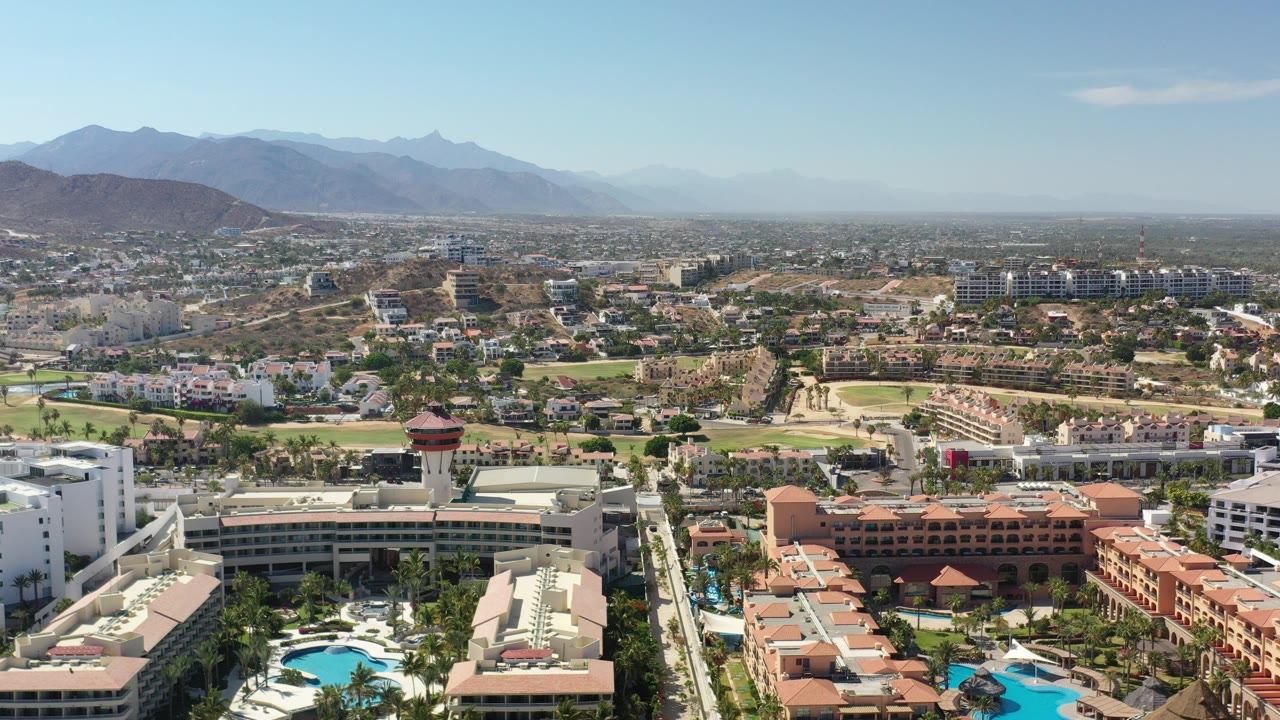 High aerial view of resort pools, beach, town, and mountains.