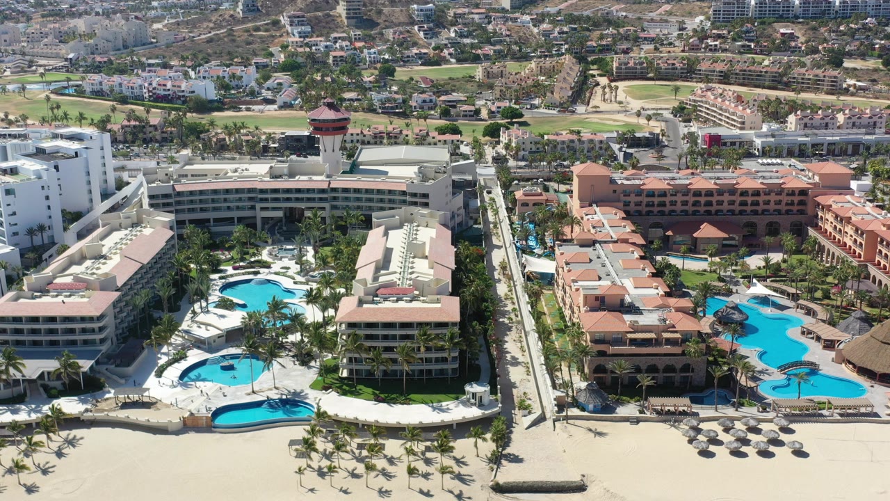 Aerial view of beachfront resort pools and hotel buildings beside sand.