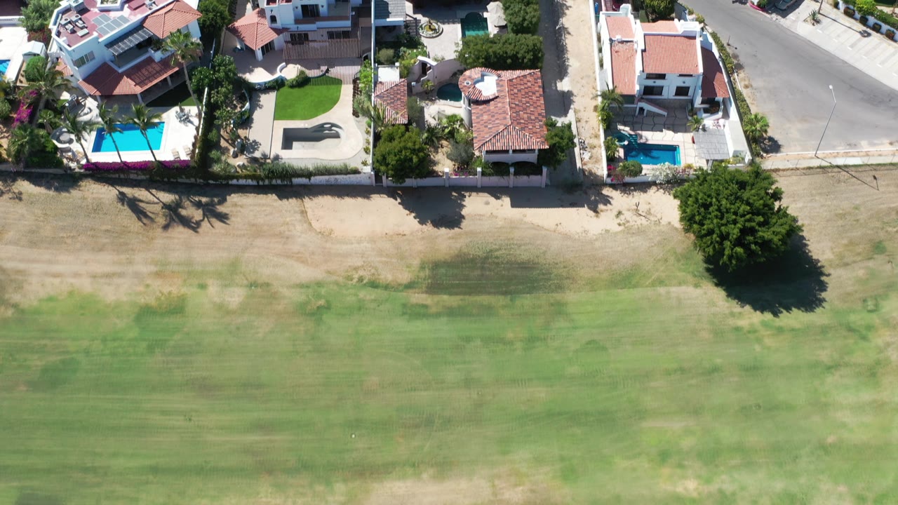 Aerial view of villas, pools, road, and patchy green ground.