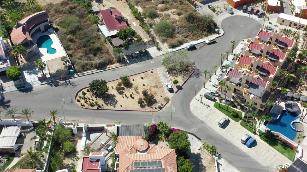 Aerial view of a curved residential road with houses, pools, dry lots, and parked cars.