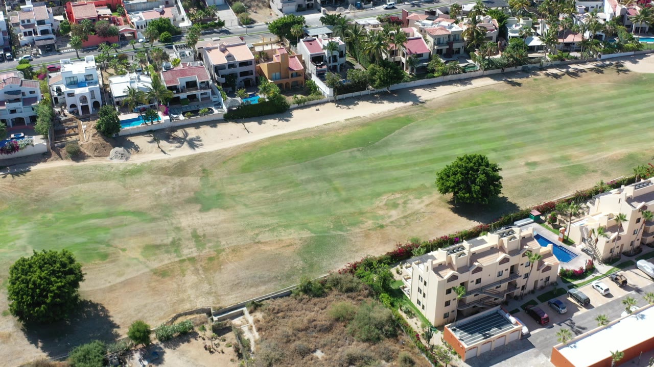 Aerial view of golf course grass beside large homes and pools.