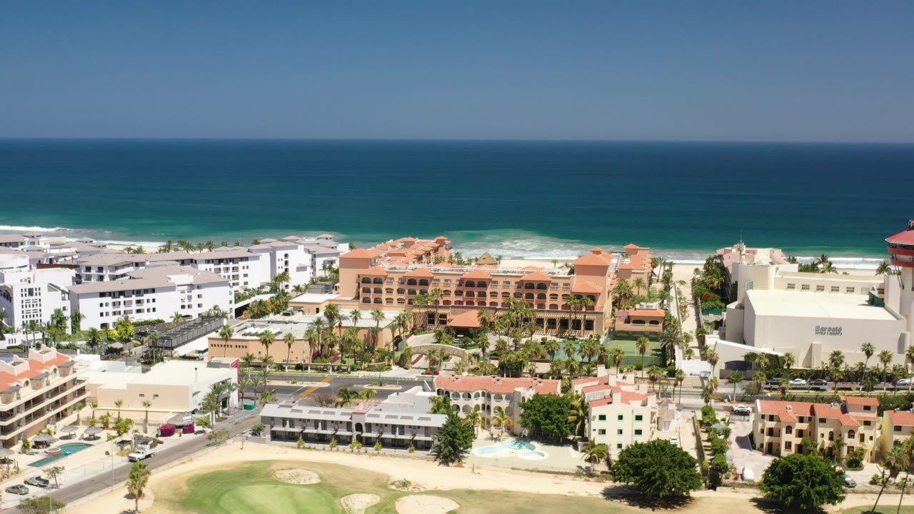 Coastal resort district with ocean, hotels, palms, and roadways.