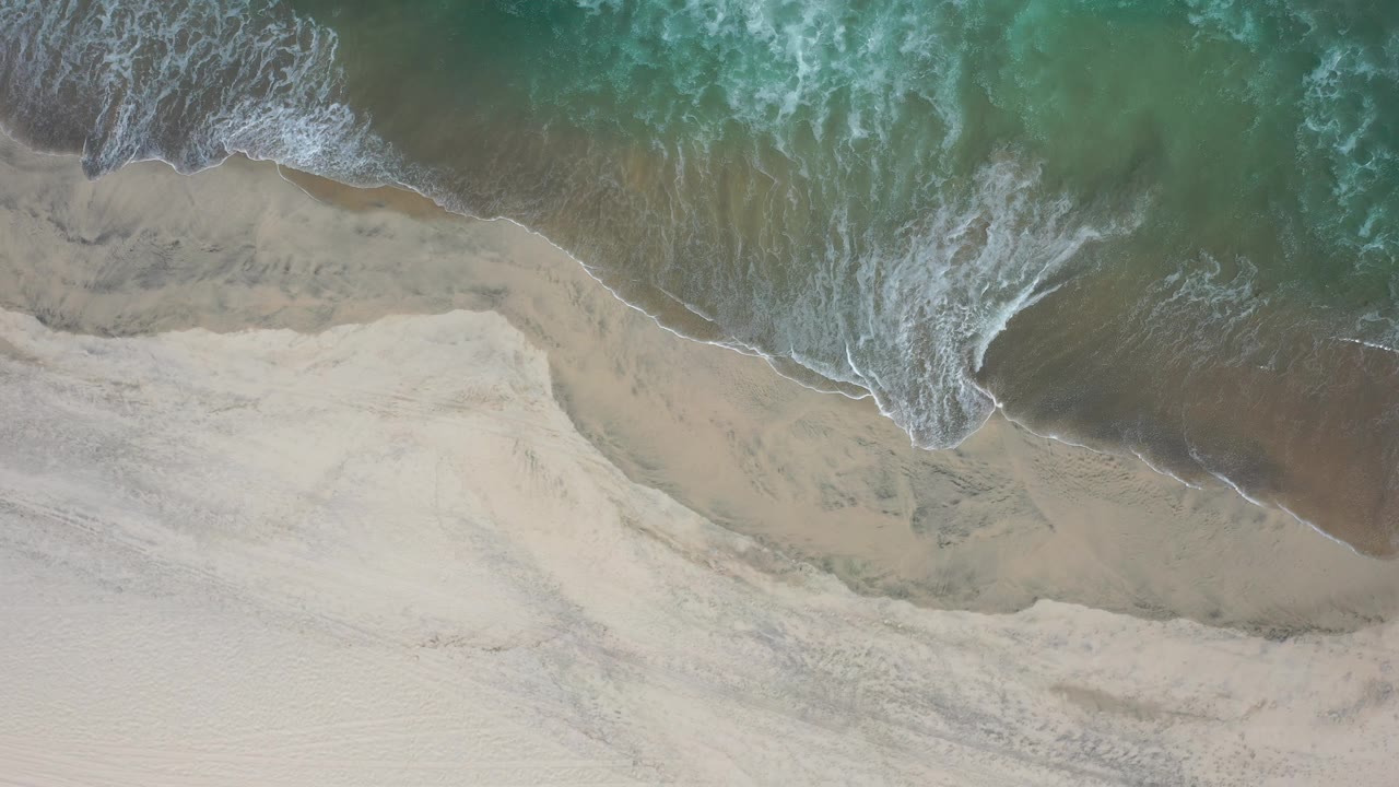 Green surf and white foam over sandy shore