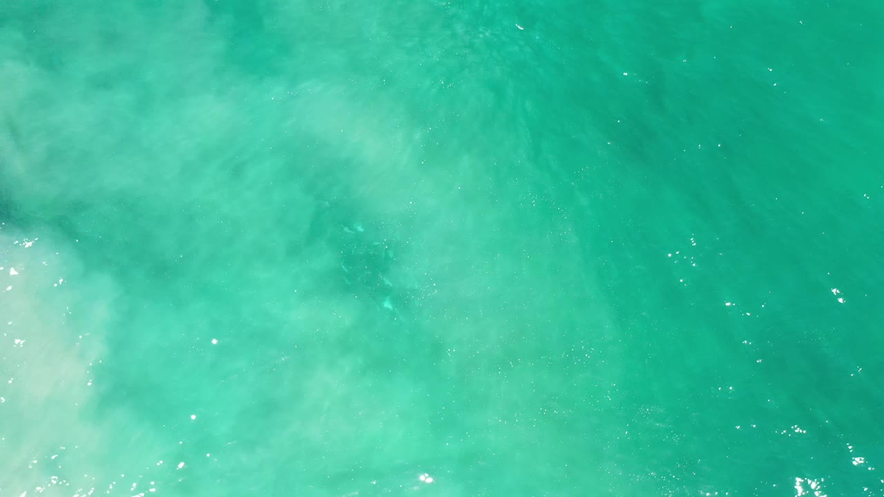 Top-down Los Cabos water surface with transparent green-blue color, faint pale clouding near the lower left, and no visible people.