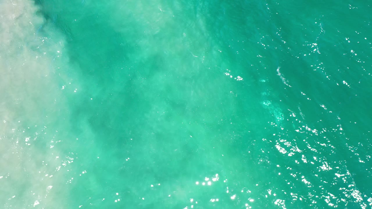 Overhead view of turquoise seawater in Los Cabos, Mexico, with pale foam entering along the left side and no visible people.