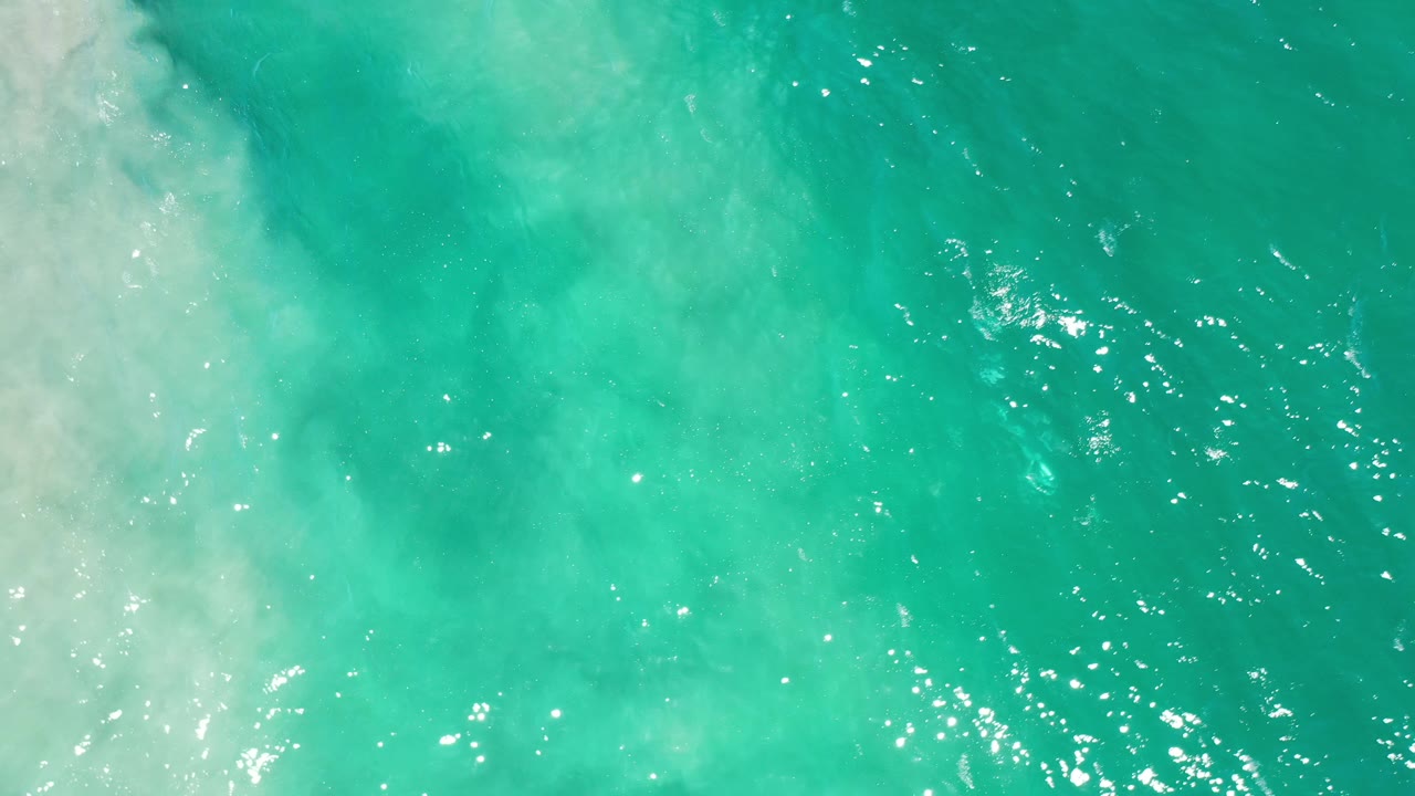 Bright turquoise water with scattered sun reflections and foam along one side.