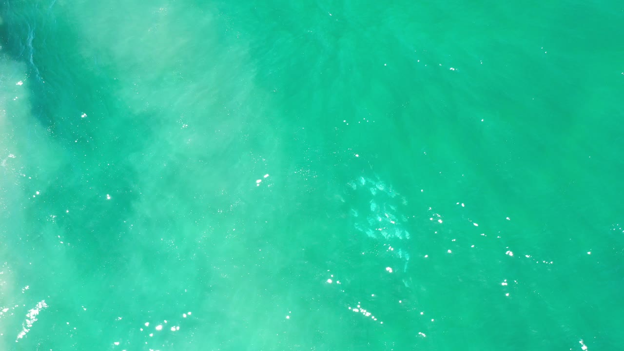 Turquoise ocean water with pale wave wash and sunlight glints.