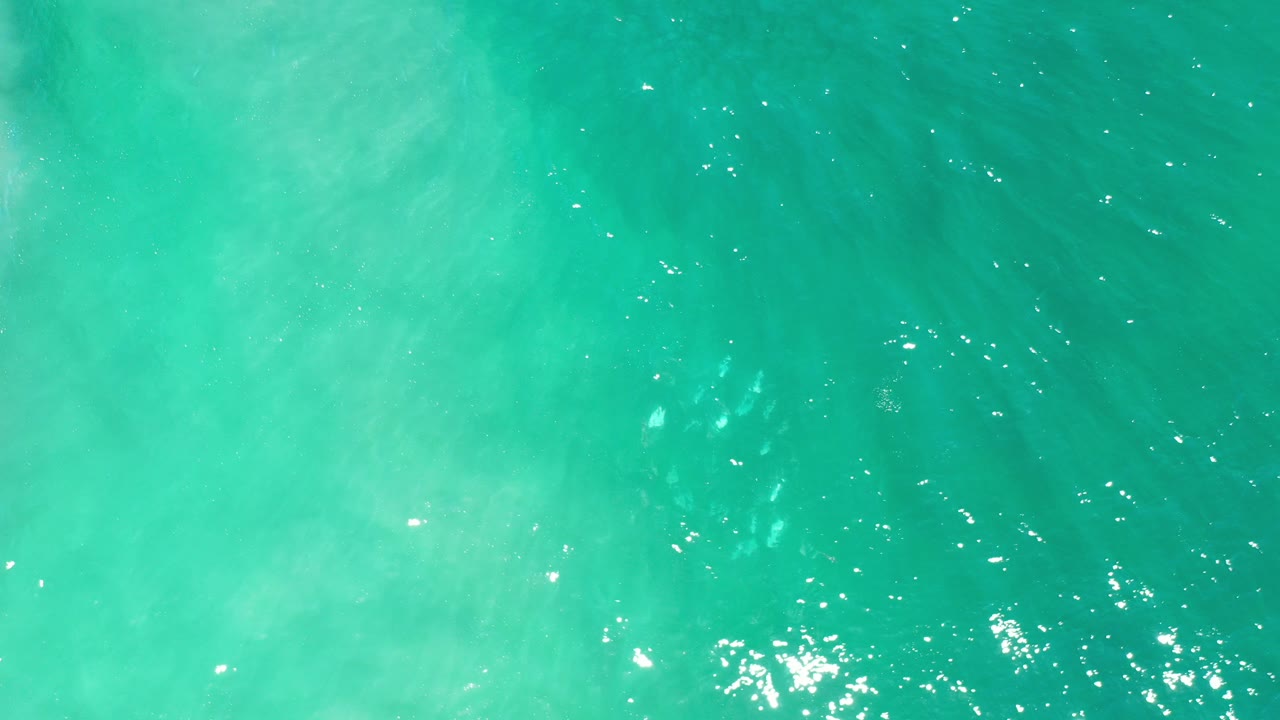 Turquoise ocean water with sun glints and pale underwater swirls.
