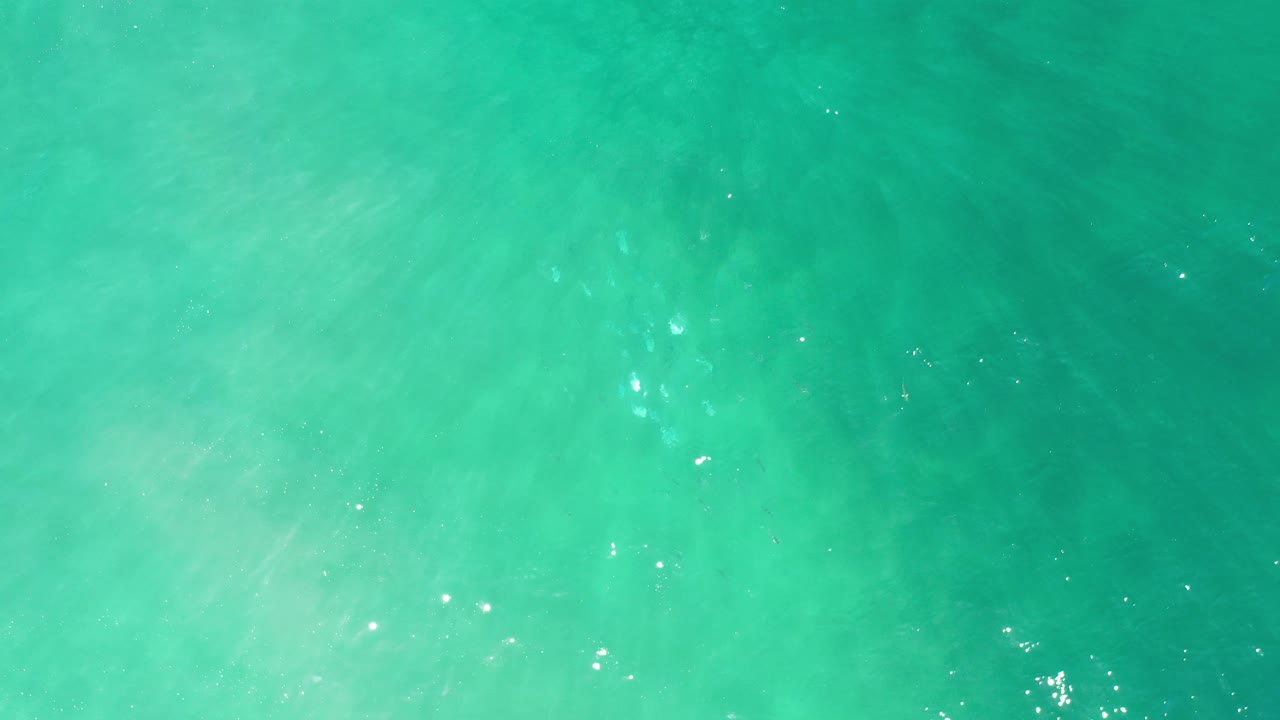 Overhead view of turquoise water in Los Cabos, Mexico, with faint ripples, light cloudy patches beneath the surface, and no visible people.