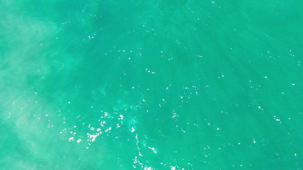Top-down view of green turquoise ocean water in Los Cabos, Mexico, with scattered bright reflections and no visible people.