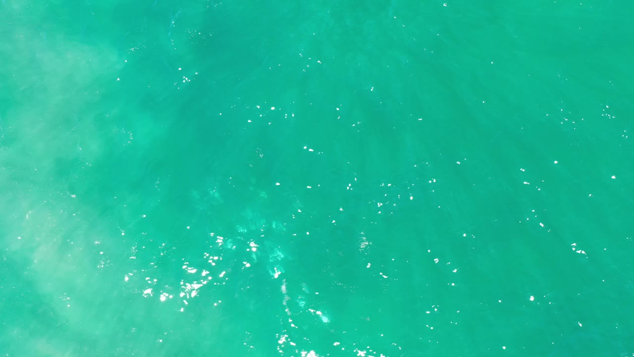 Aerial-looking frame of Los Cabos green ocean water with muted pale patches beneath the surface and no visible people.
