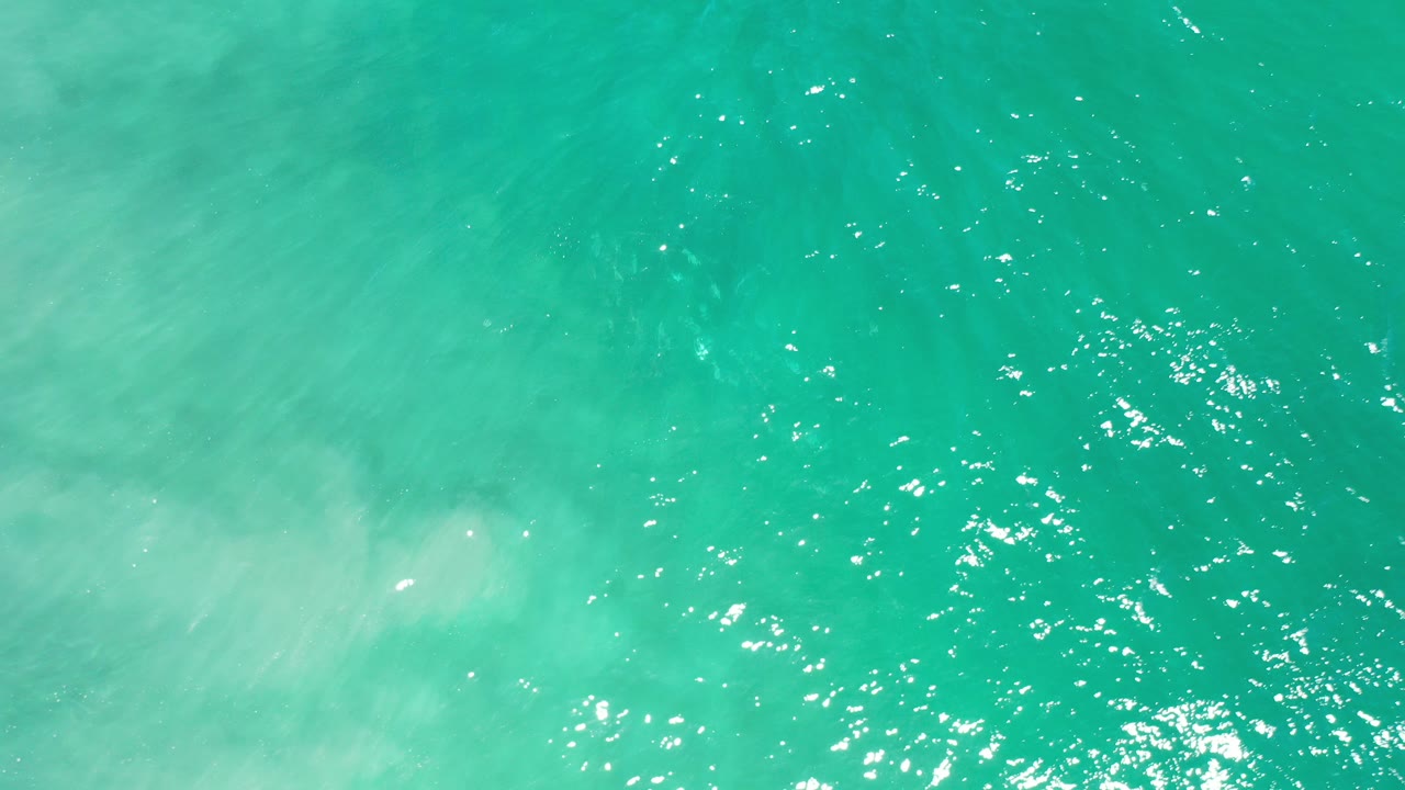 Overhead view of turquoise ocean water in Los Cabos, Mexico, with fine ripples, scattered white reflections, and no visible people.
