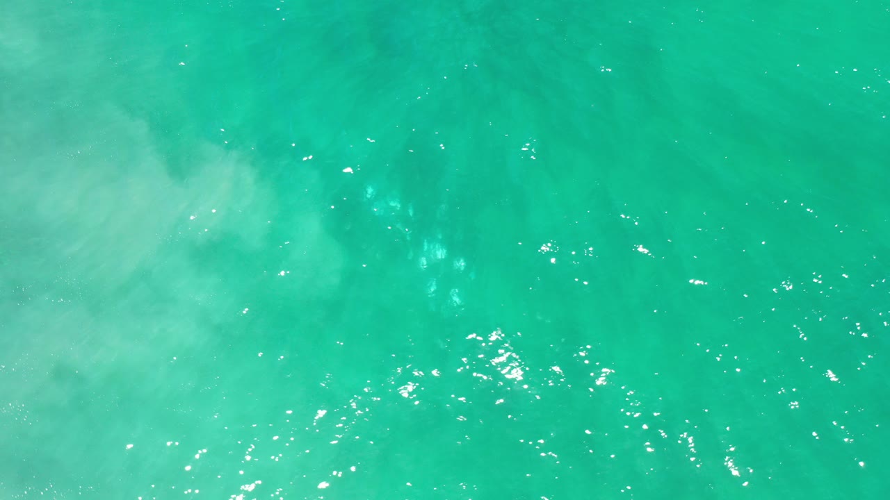 Top-down view of turquoise seawater in Los Cabos, Mexico, with scattered white sparkle on the surface and no visible people.