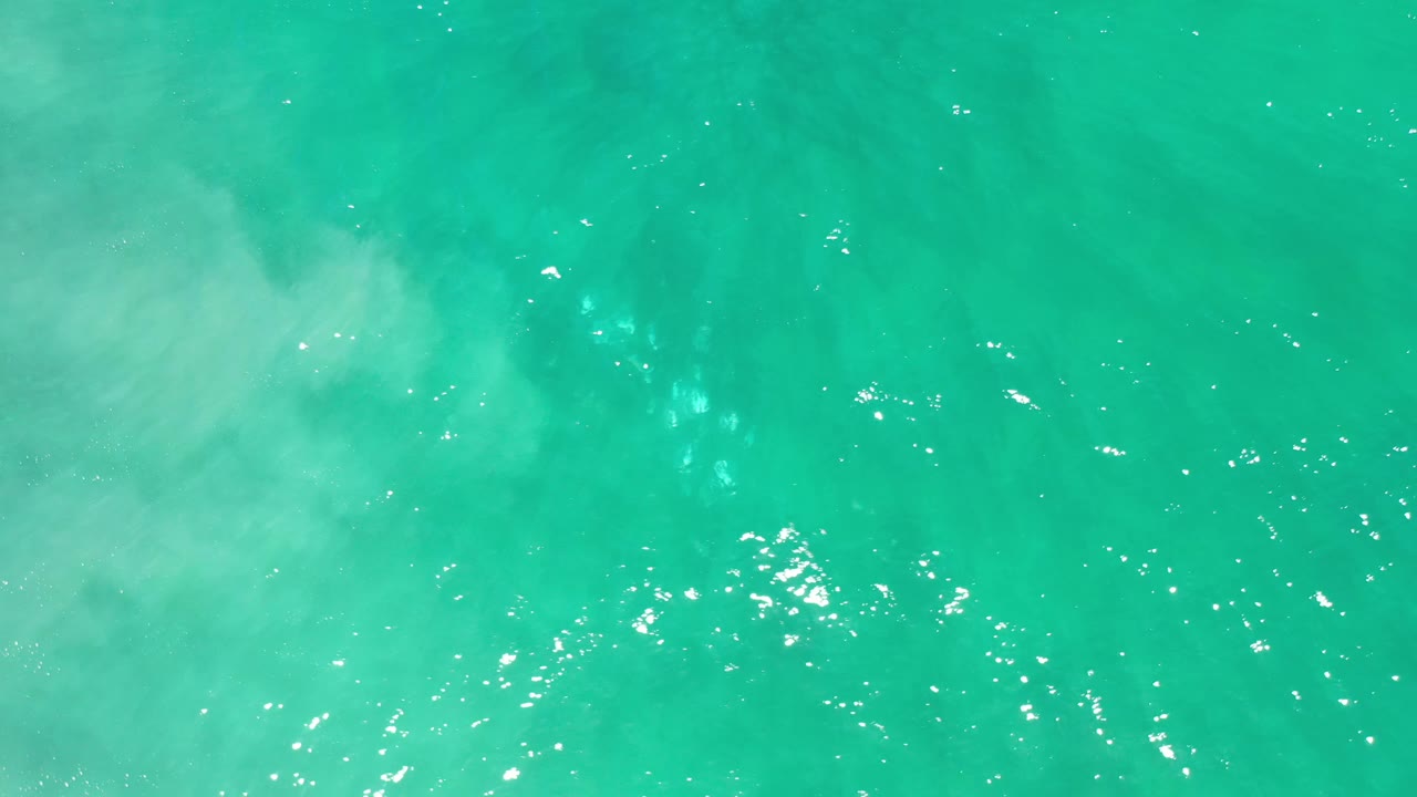 Overhead Los Cabos water frame with pale cloudy areas under the aquamarine surface, bright ripple highlights, and no visible people.