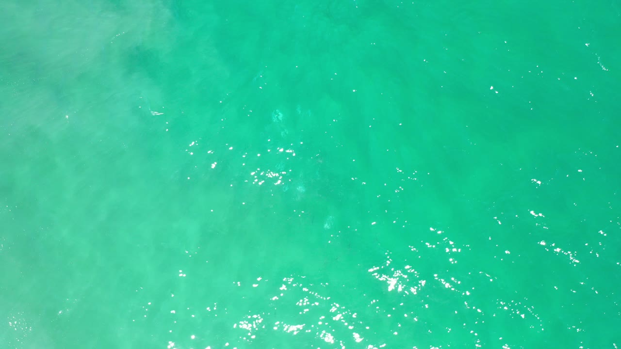 Opening frame of green turquoise ocean water in Los Cabos, Mexico, seen from above with scattered sun sparkle and no visible people.