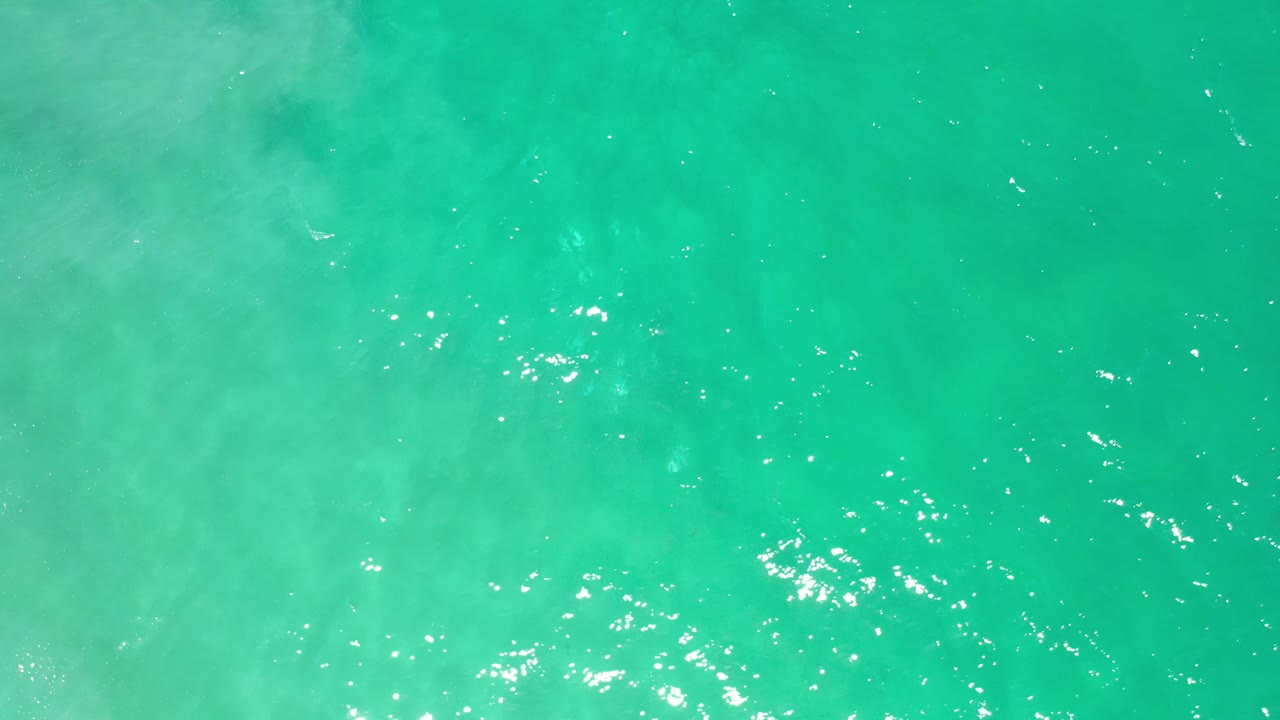 Aerial-looking frame of Los Cabos green ocean water with soft pale patches under the surface and no visible people.