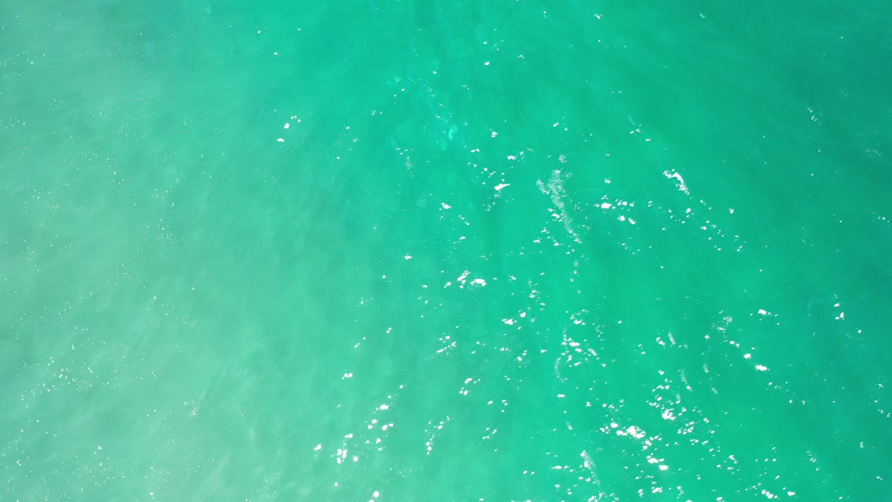 Overhead view of turquoise ocean water in Los Cabos with pale surf wash entering the frame and no visible people.