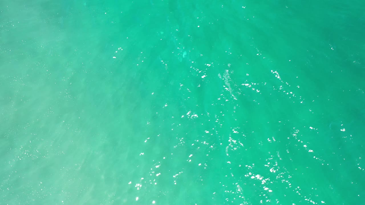 Overhead Los Cabos water frame with scattered white sunlight highlights across turquoise ripples and no visible people.