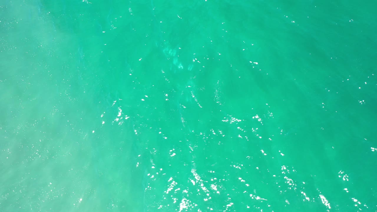 Turquoise ocean surface with cloudy pale wave wash.