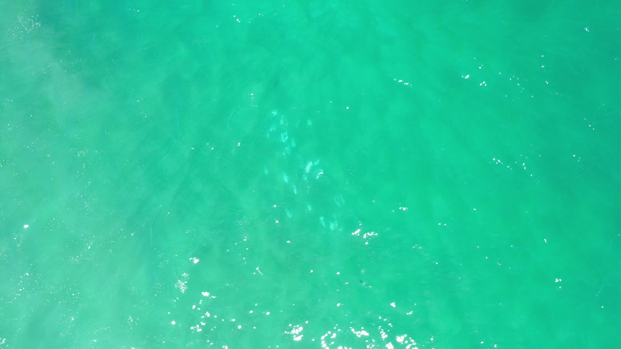 Overhead view of clear turquoise water over pale sand in Los Cabos, Mexico, with faint ripples, scattered highlights, and no visible people.