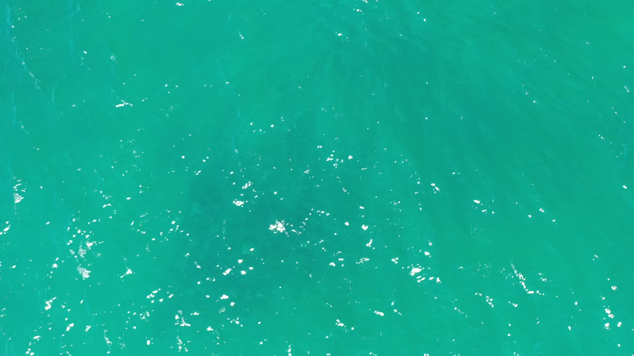Top-down Los Cabos sea frame showing green-blue water, fine ripples, and small bright reflections with no visible people.