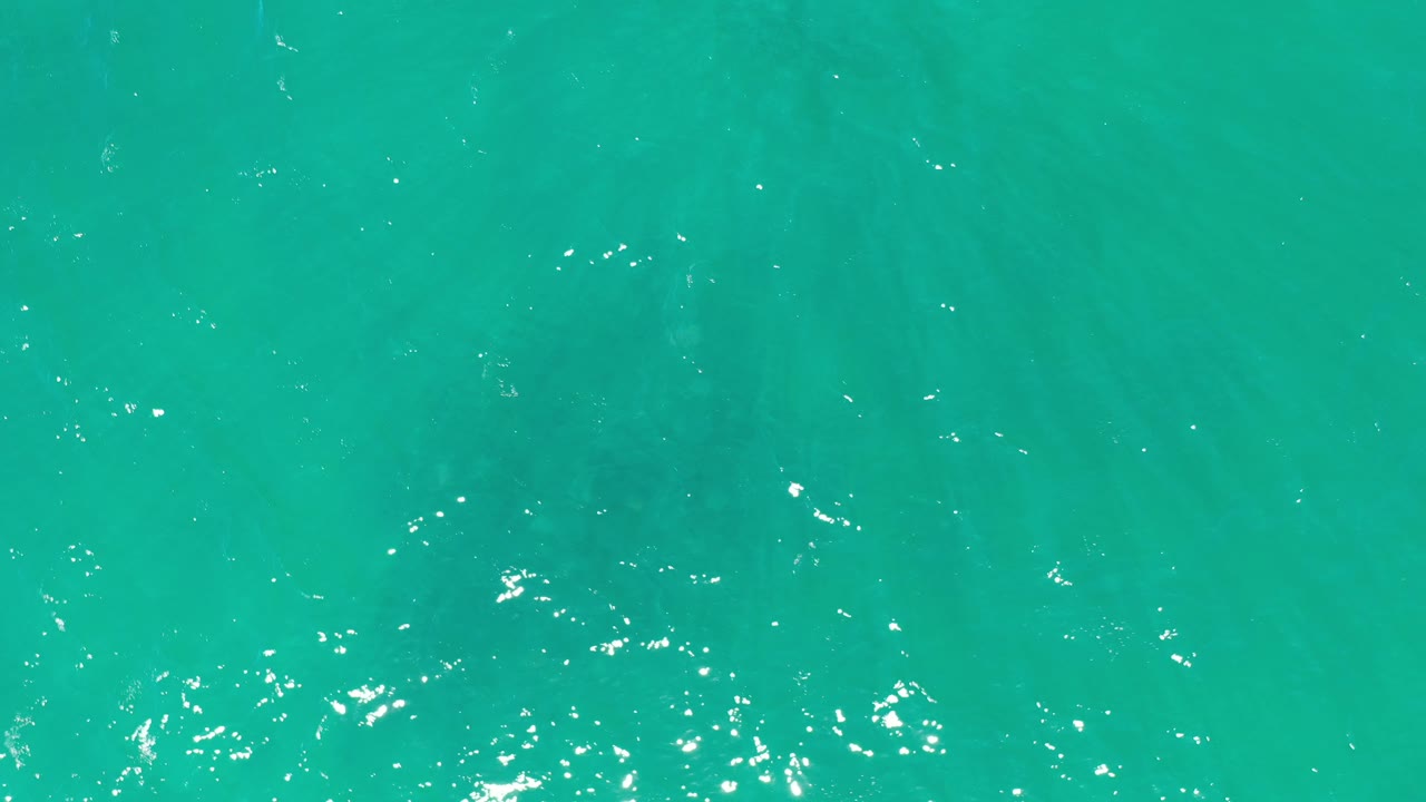 Turquoise sea surface with faint darker areas below.