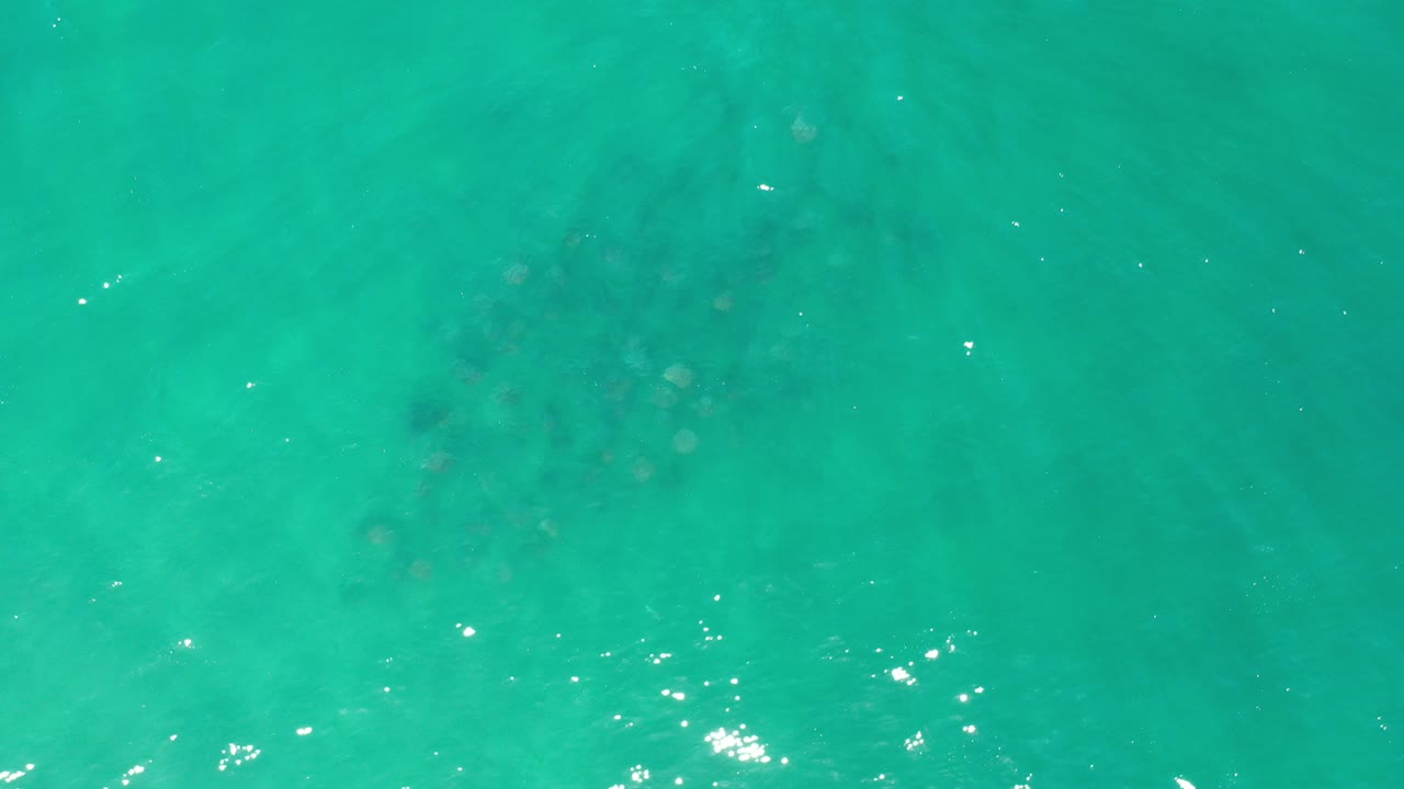 Top-down view of turquoise green water near Los Cabos, Mexico, with sun flecks on the surface, faint underwater shapes, and no visible people.
