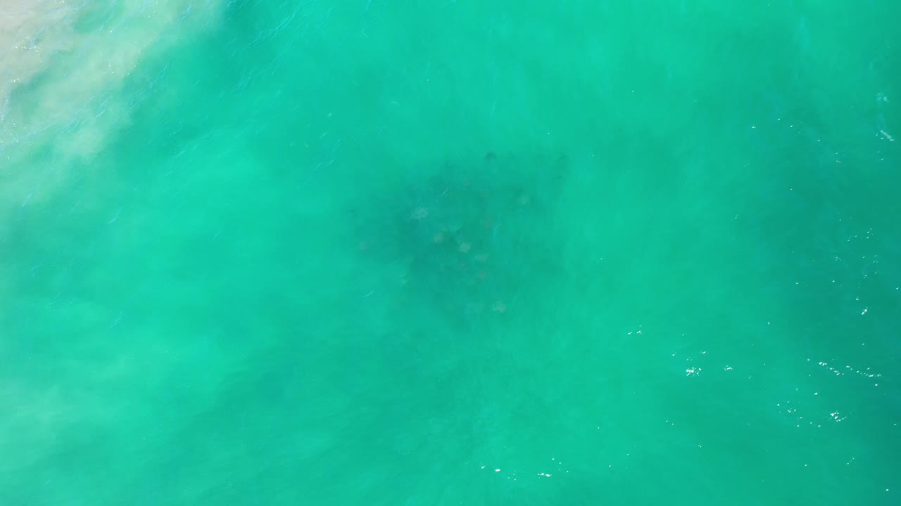 Teal ocean surface in Los Cabos, Mexico, with faint white ripples across the middle and a darker underwater patch, no visible people.