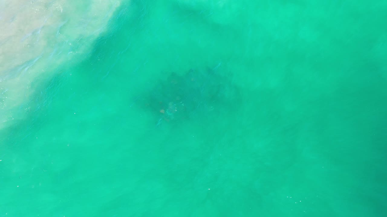 Bright turquoise water with soft surf wash and shadowy underwater areas.