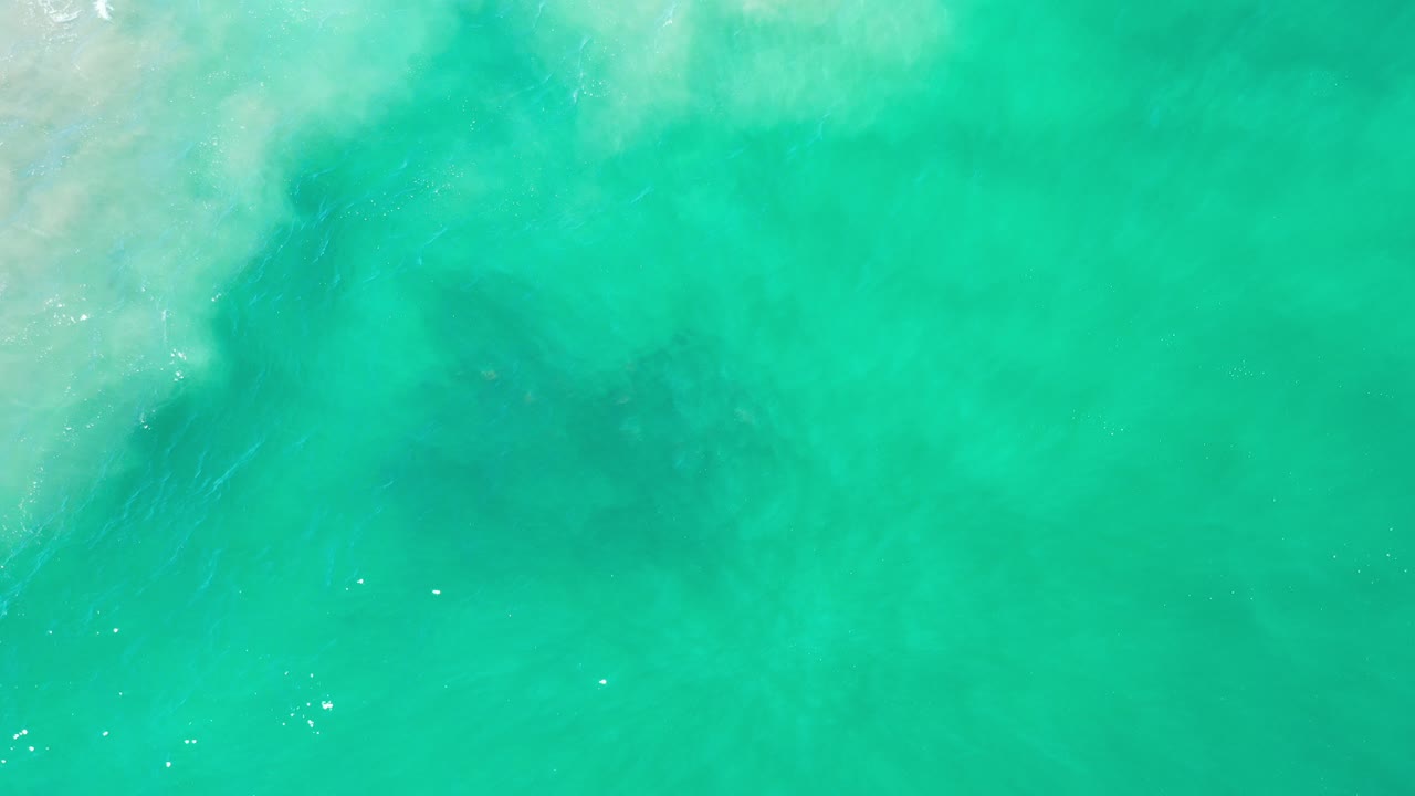 Overhead turquoise ocean water in Los Cabos, Mexico, with pale foam spreading from the upper left and no visible people.