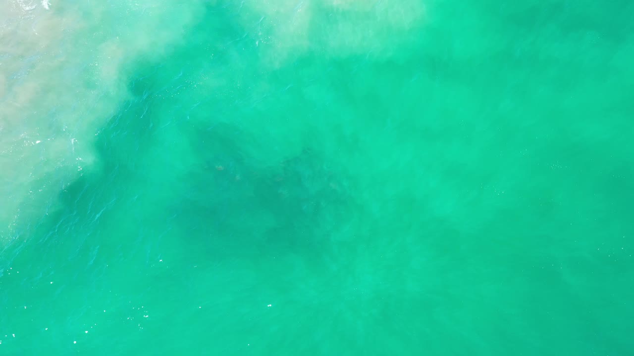 Overhead green-blue water in Los Cabos, Mexico, with faint foam near the top left, darker patches below the surface, and no visible people.
